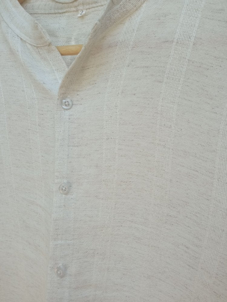 Close-up of a light gray textured shirt with buttons on a wooden hanger.