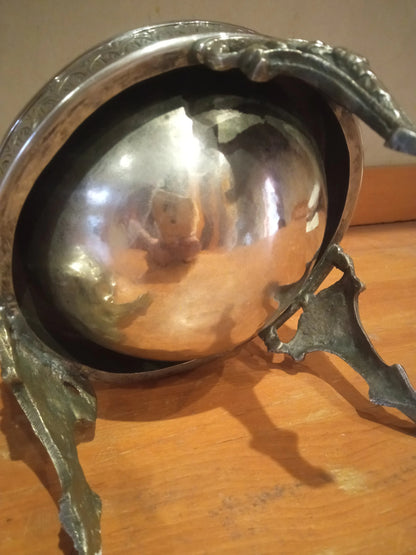 Decorative silver bowl with ornate metal stand on a wooden surface