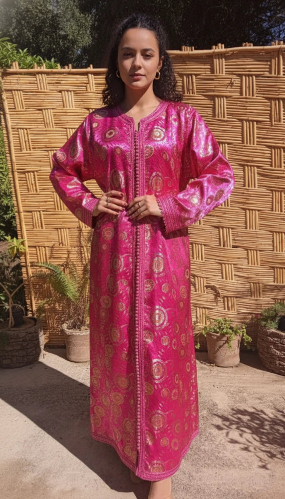 Woman wearing a pink traditional Moroccan kaftan dress vintage with gold patterns against a woven wall.