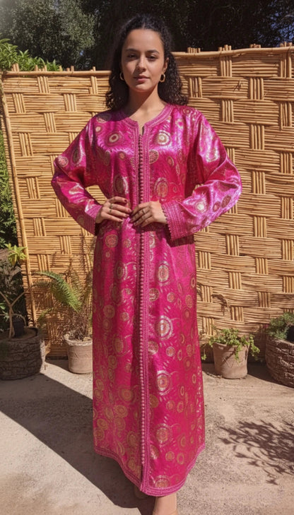 Woman wearing a pink traditional Moroccan kaftan dress vintage with gold patterns against a woven wall.