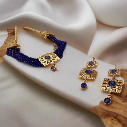 A gold choker necklace with blue beads and additional gold beads, displayed on a white fabric surface.