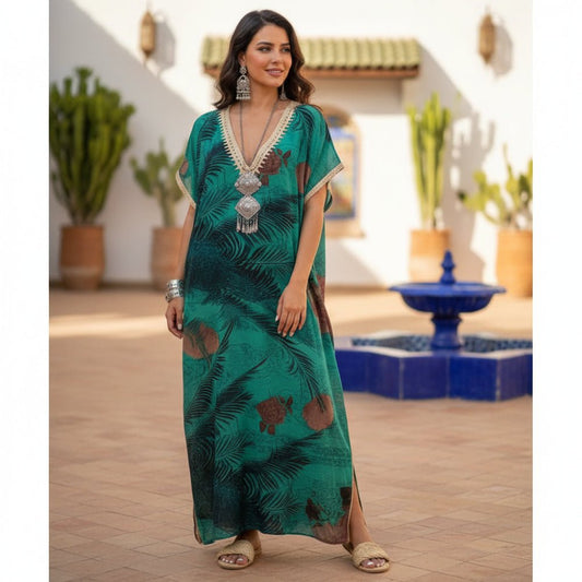 Woman in a green gandoura standing in a decorative outdoor setting with plants and a fountain.