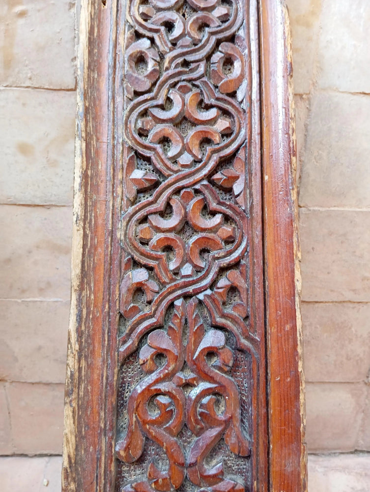 Carved wooden panel with intricate patterns on a stone wall background