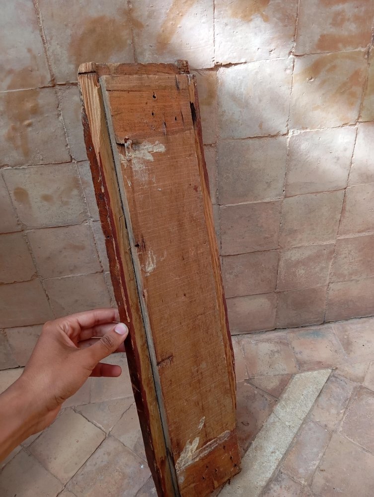 Hand holding a wooden panel against a tiled wall