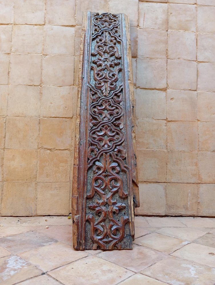 Decorative wooden panel with intricate carvings against a stone wall.
