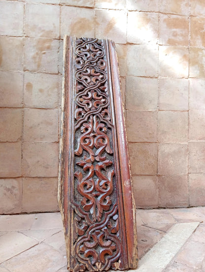 Decorative wooden panel with intricate carvings against a stone wall.