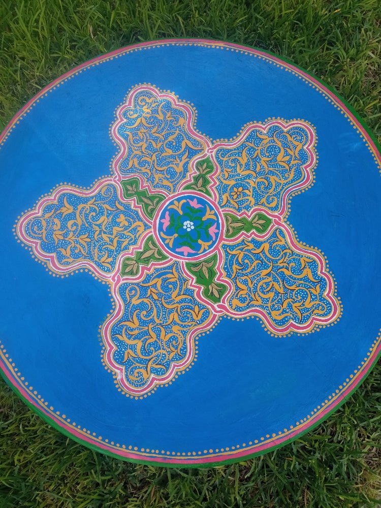Decorative round accent table handpainted with intricate patterns on a grassy background