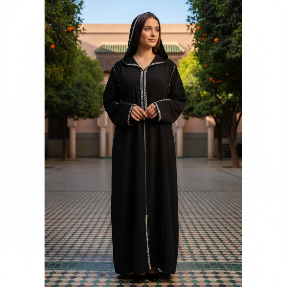 Woman in a black moroccan djellaba standing in a courtyard with trees and a building in the background.