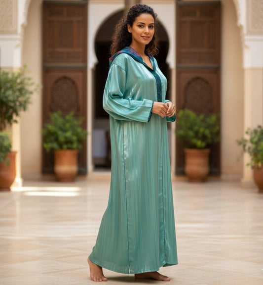 Woman in a teal djellabadress standing in a sunlit courtyard with plants and wooden doors.