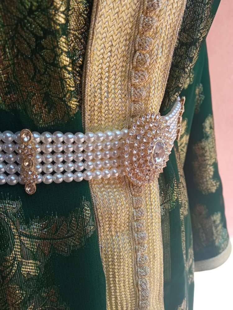 Close-up of a decorative belt with pearls and crystals on a green embroidered fabric background.