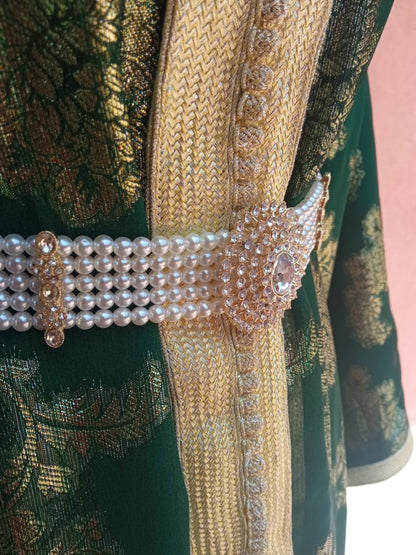 Close-up of a decorative belt with pearls and crystals on a green embroidered fabric background.