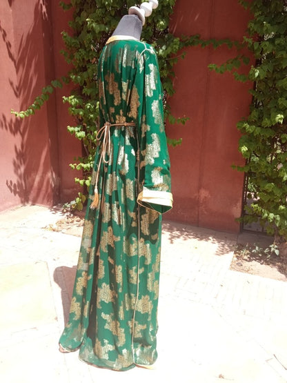 Green and gold patterned dress on a mannequin against a red wall with greenery.