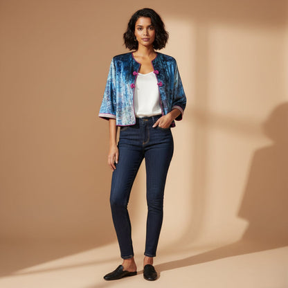 Woman wearing a blue patterned jacket, white top, and dark jeans on a beige background