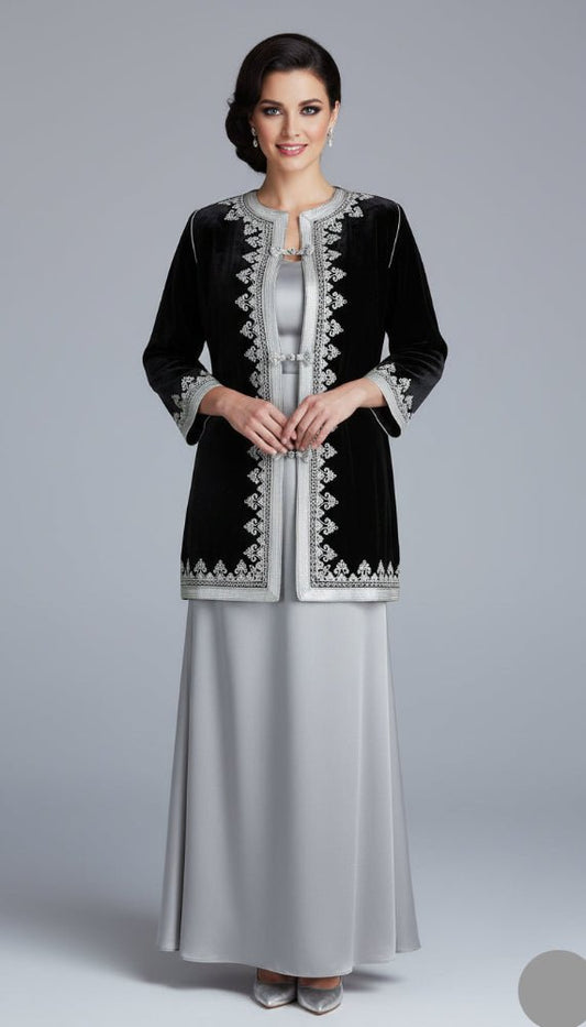 Woman wearing a black embroidered jacket over a silver dress on a gray background