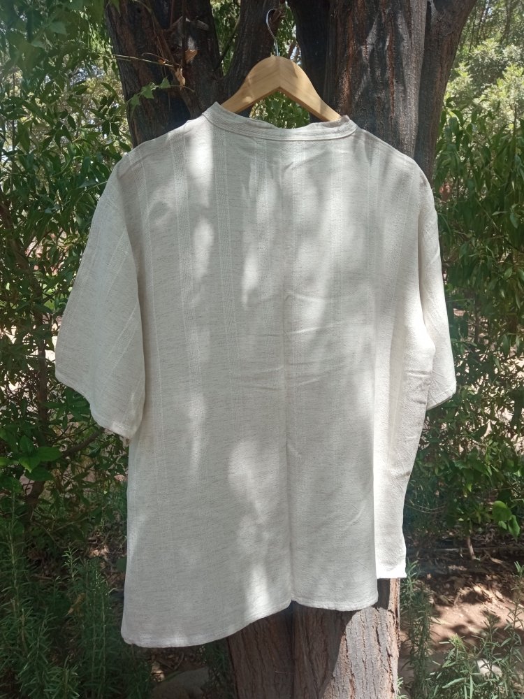 White shirt on a hanger against a natural background with trees and foliage.
