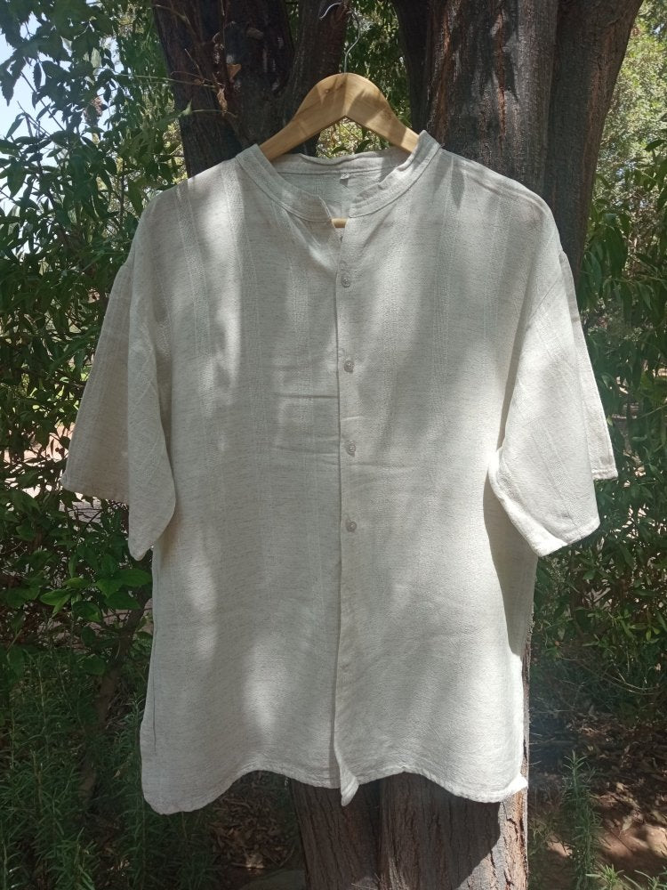 Light-colored shirt on a hanger against a natural background with trees and foliage.