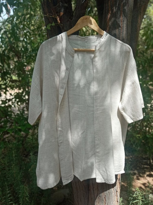 Light-colored shirt on a hanger against a natural background with trees and foliage.