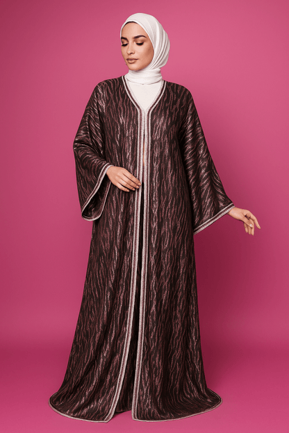 Woman wearing a long, patterned dress with a hood against a pink background