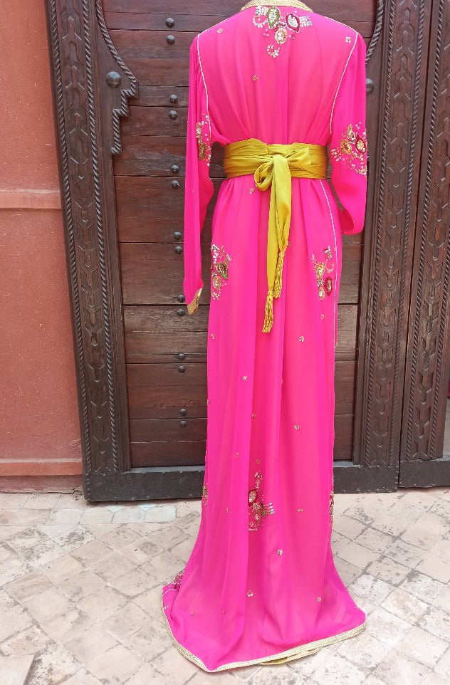 Pink embroidered dress with a green belt displayed against a wooden door.