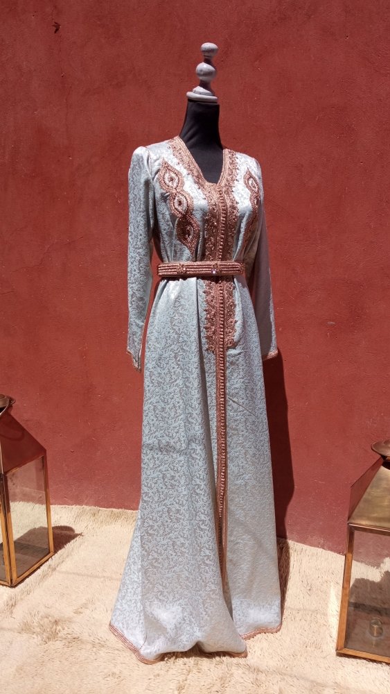 Long, elegant caftan Moroccan dress with intricate patterns on a mannequin against a red wall.