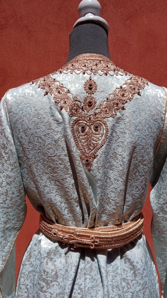 Mannequin wearing a light-colored dress with intricate brown embroidery on the back against a red background