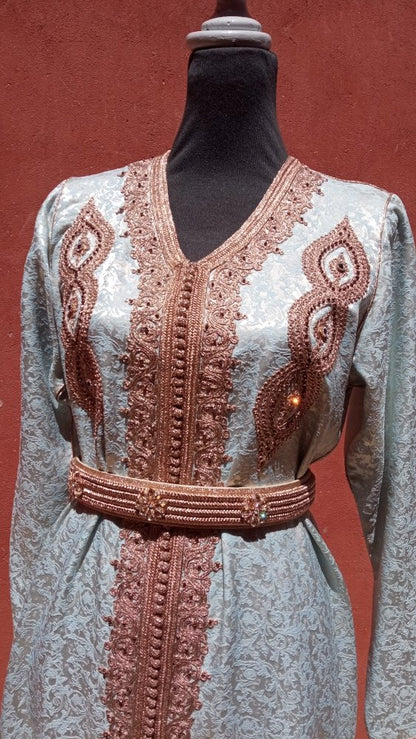 Decorative Moroccan caftan dress with intricate embroidery on a mannequin against a red background