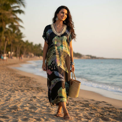Woman walking on a beach wearing a colorful kaftan dress, gandora and holding a woven bag.