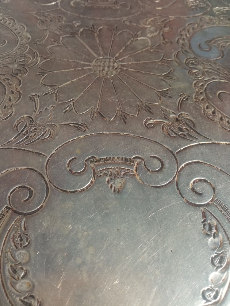 Close-up of an engraved metal tray with floral and scroll designs.