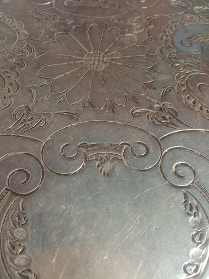 Close-up of an engraved metal tray with floral and scroll designs.