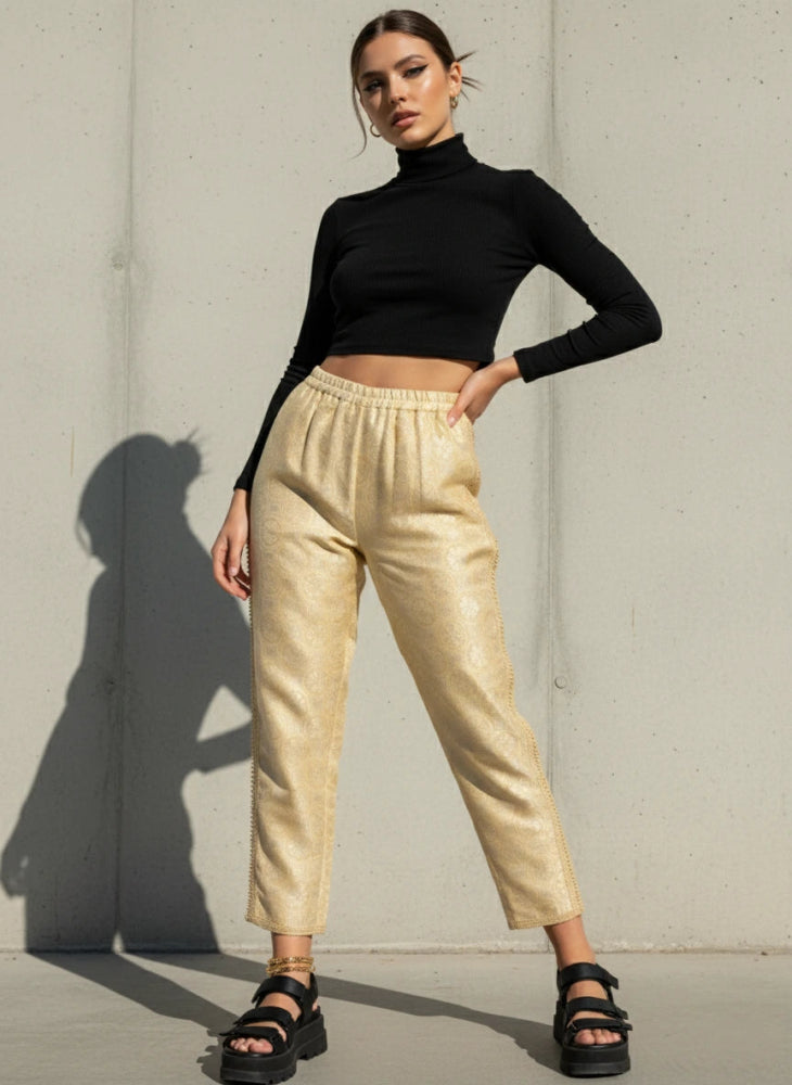 Woman wearing a black turtleneck and ivory brocade Moroccan vintage pants against a gray wall.