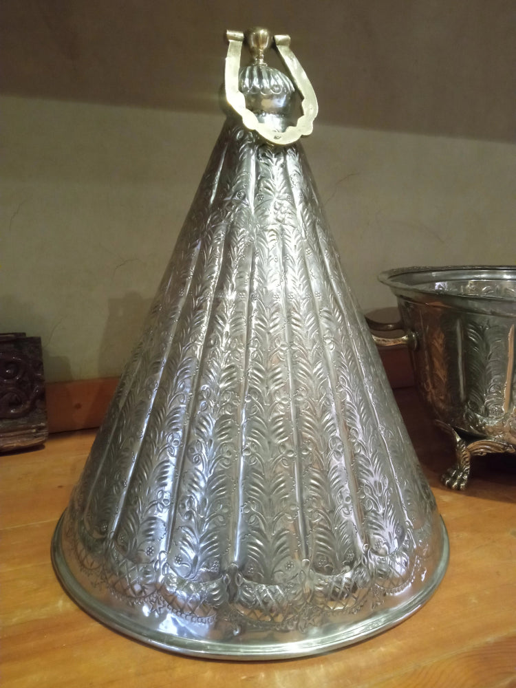 Decorative silver metal cone with embossed design on a wooden surface