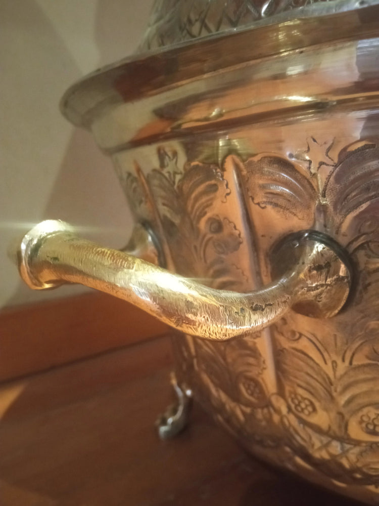 Decorative metalmoroccan tajine with intricate designs and a handle on a brass surface.