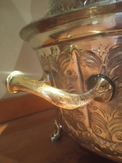 Decorative metalmoroccan tajine with intricate designs and a handle on a brass surface.