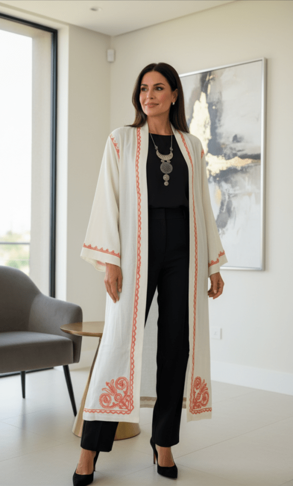 Woman in a long, light-colored coat with red patterns standing in a modern interior setting.
