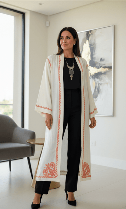 Woman in a long, light-colored coat with red patterns standing in a modern interior setting.