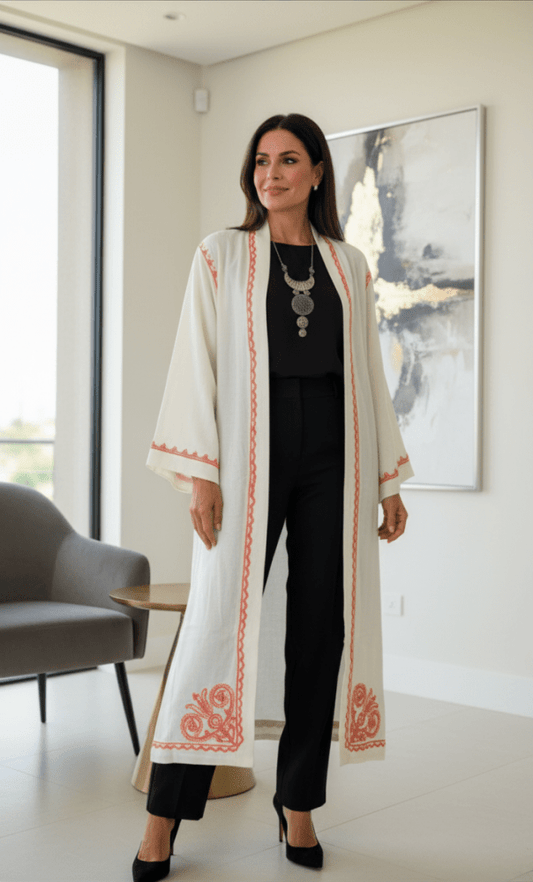 Woman in a long, light-colored coat with red patterns standing in a modern interior setting.